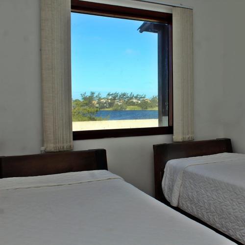 two beds sitting in a room with a window at Pousada do Albatroz in Cabo Frio