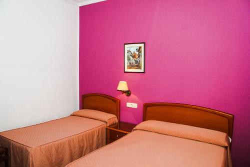 マドリードにあるPensión Numanciaのピンクの壁の客室で、ベッド2台が備わります。