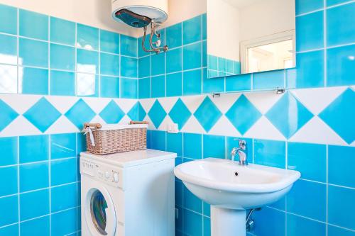 bagno piastrellato blu con lavatrice e lavandino di Poggio Dei Fiori Appartamento G2 a Olbia