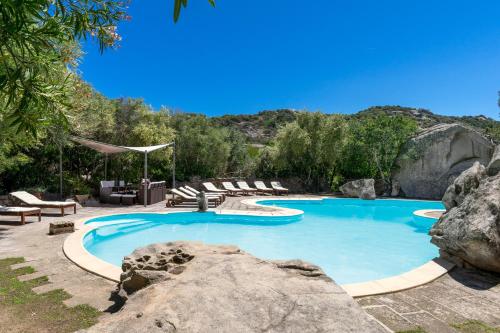 a swimming pool with chairs and a large rock at Villa Nuraghe in Porto Rotondo