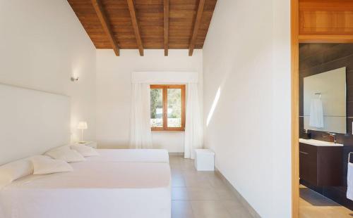 a white bedroom with two beds and a bathroom at Sa Garriga in Ariany