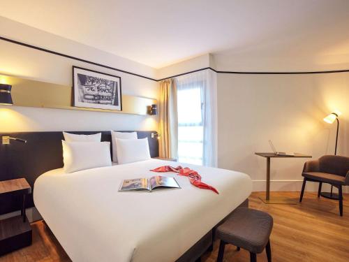 a hotel room with a large white bed with a book on it at Mercure Paris Saint-Ouen in Saint-Ouen