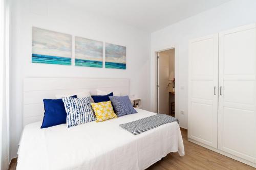 a white bedroom with a white bed with blue pillows at Apartamento Luna in Barbate