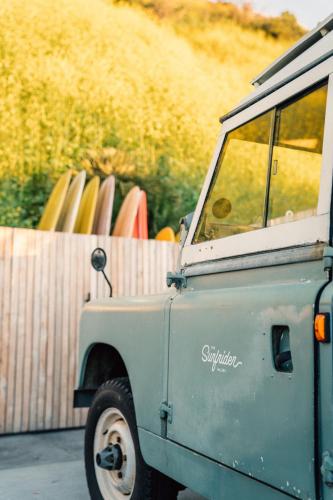 an old car parked next to a fence with surfboards at The Surfrider Malibu in Malibu