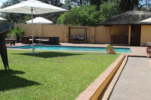 a swimming pool with an umbrella and some grass at Casa Mia Lodge & Restaurant in Blantyre