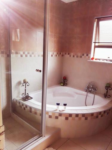 a bathroom with a bath tub with a shower at Rocky Ridge Guest House SELF Catering - No alcohol allowed in Roodepoort