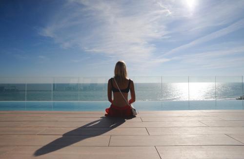 a woman sitting on the edge of a building looking out at the ocean at Playa Grande by Tropical - Adults Only in Gavà