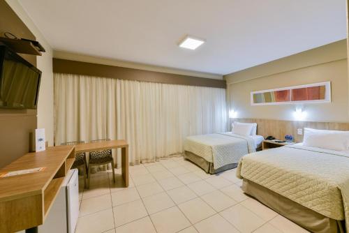 a hotel room with two beds and a desk at Plaza Inn Augustus in Goiânia