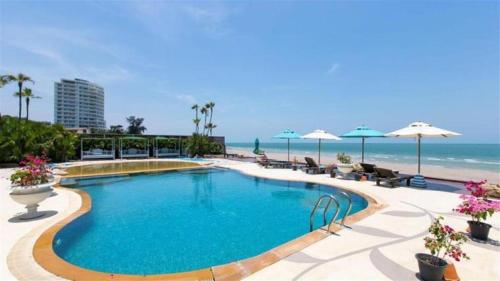 a swimming pool next to the beach with umbrellas at My Resort Family Condo Huahin in Hua Hin