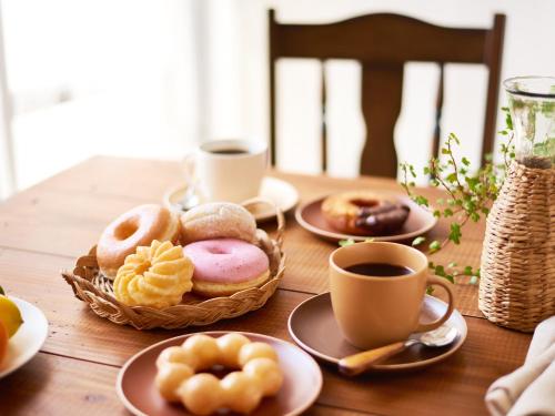 a wooden table with plates of donuts and cups of coffee at Sotetsu Fresa Inn Nagoya Sakuradoriguchi in Nagoya