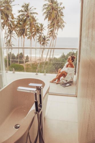 a woman sitting on a window sill next to a bath tub at The Habitat Kosgoda by Asia Leisure in Bentota