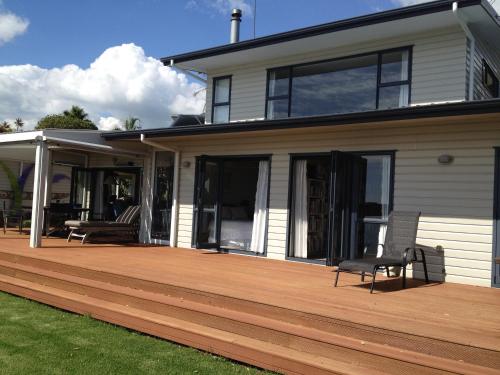 uma casa com um deque de madeira com duas cadeiras em Absolute Waterfront Serenity Near Auckland em Clarks Beach