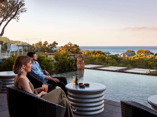 a man and woman sitting on a patio overlooking the ocean at Pullman Bunker Bay Resort Margaret River in Dunsborough