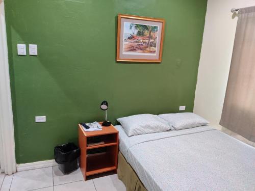 a bedroom with a green wall with a bed and a night stand at Woodbrook on the Avenue in Port-of-Spain