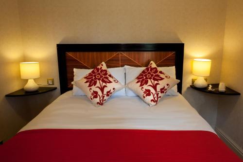 a bed with red and white pillows and two lamps at Royal Court Hotel & Spa Coventry in Coventry