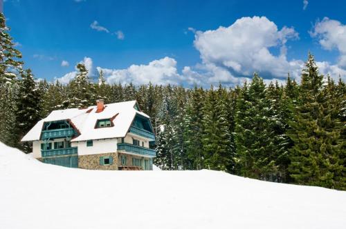 a house covered in snow in front of trees at Apartma Borovnica Rogla in Vitanje