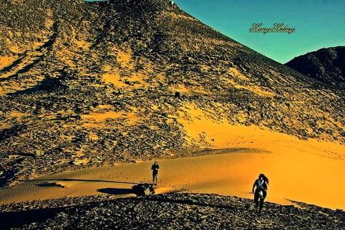 two people walking on the sand near a mountain at Safari Abu Simbel in Abu Simbel