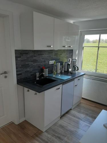 a kitchen with white cabinets and a sink and a window at Backbord in Wangerland