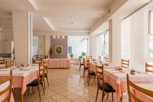 a dining room with tables and chairs and a kitchen at Hotel Alda in Cervia