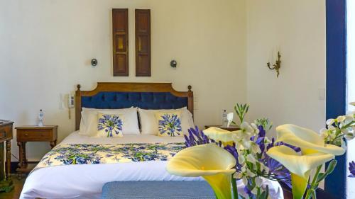 a bedroom with a bed with blue and white pillows and flowers at Hostería Hacienda Pinsaqui in Otavalo