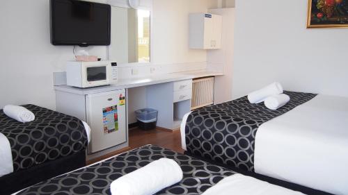 a small room with two beds and a desk at Queanbeyan Motel in Queanbeyan