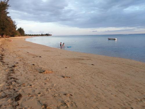 two people standing on a beach with a boat in the water at Villa dauphin in Bel Ombre