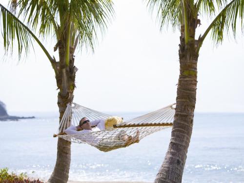 a man laying in a hammock between two palm trees at Mandarin Oriental, Sanya in Sanya