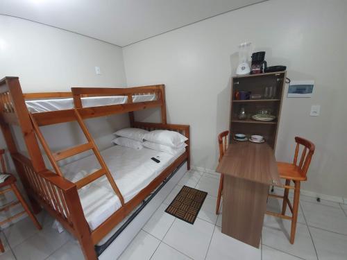 a bedroom with a bunk bed and a table and a desk at Kitnet Praia da Vila Imbituba in Imbituba