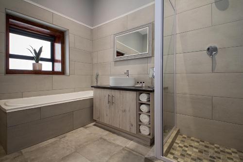 een badkamer met een wastafel, een bad en een spiegel bij Merino Stal Guest Farm in Ermelo