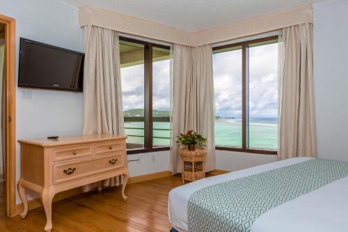a bedroom with a bed and a tv and windows at Alupang Beach Tower in Tamuning
