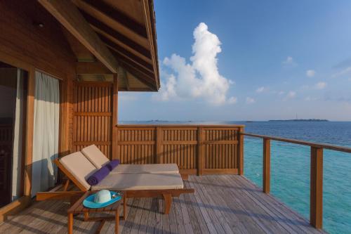 a deck with a bench and a table on the water at Vilamendhoo Island Resort & Spa in Dhangethi