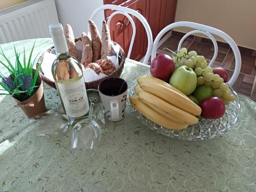 a table with a glass bowl of fruit and a bottle of wine at Yellow Apartmanház in Bük