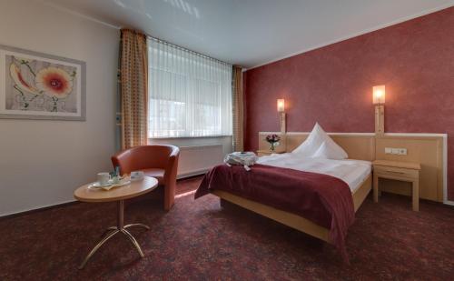ラントシュトゥールにあるHotel Merkurのベッド、テーブル、椅子が備わるホテルルームです。