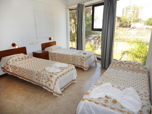 una camera d'albergo con tre letti e una grande finestra di Hotel Reviens a Villa Gesell