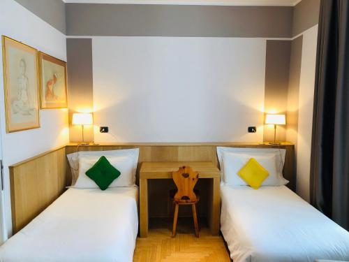 two beds in a room with a table and a chair at Hotel Alla Posta in Saint Vincent