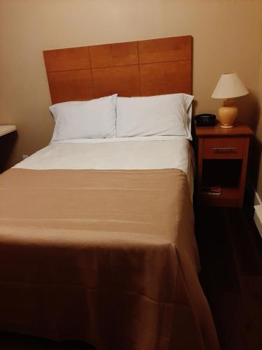 a bed with a wooden headboard and a nightstand with a lamp at Motel LA RÉFÉRENCE in Trois-Rivières