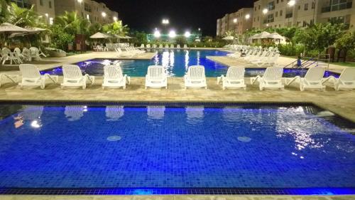 einen Pool in der Nacht mit weißen Liegestühlen vor dem Hotel in der Unterkunft Flat térreo Palm Village Acqua Porto de Galinhas in Porto De Galinhas