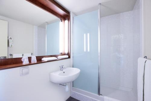 La salle de bains blanche est pourvue d'un lavabo et d'une douche. dans l'établissement Campanile Montbéliard - Sochaux, à Sochaux