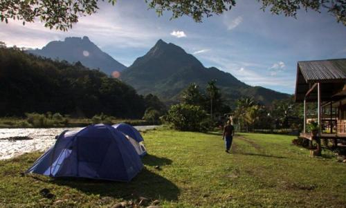a man standing next to a tent in a field at Tambatuon Homestead in Kota Belud