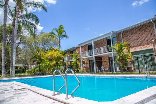 a swimming pool in front of a building with palm trees at The Select Inn Gosford in Gosford