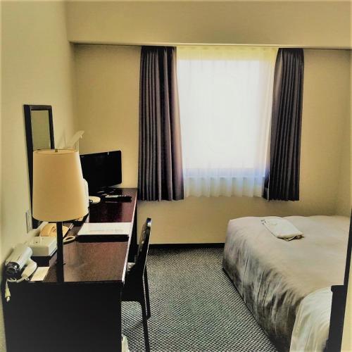 a hotel room with a desk and a bed and a window at Ishinomaki Grand Hotel in Ishinomaki