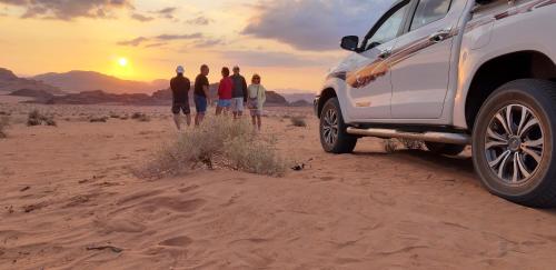 a group of people standing in the desert watching the sunset at bedouin future camp in Wadi Rum