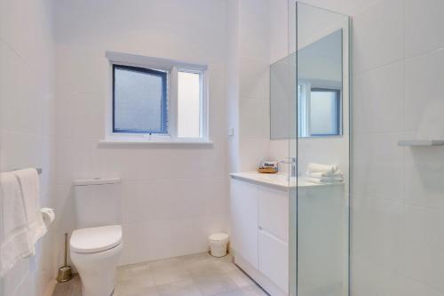 a white bathroom with a toilet and a glass shower at Bayview Apartments in Adelaide