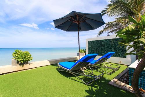 two chairs and an umbrella on a lawn with the ocean at Samui Resotel Beach Resort in Chaweng