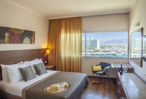 a hotel room with a bed with a desk and a window at Caesar Premier Eilat Hotel in Eilat