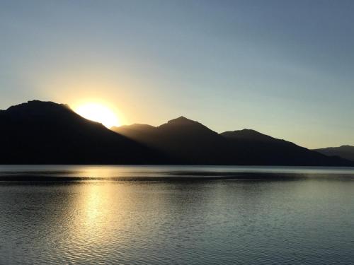 a sunset over a lake with mountains in the background at Kingfisher de los Andes in Villa Meliquina