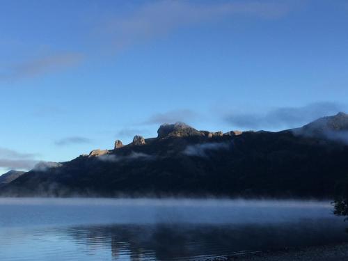 a misty lake with a mountain in the background at Kingfisher de los Andes in Villa Meliquina