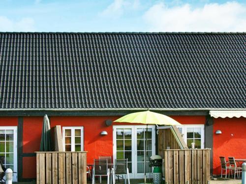 a red building with a table and an umbrella at 4 person holiday home in Aakirkeby in Åkirkeby