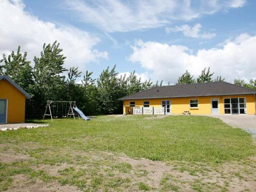 una casa amarilla con parque infantil en el patio en 12 person holiday home in H jslev, en Bøstrup