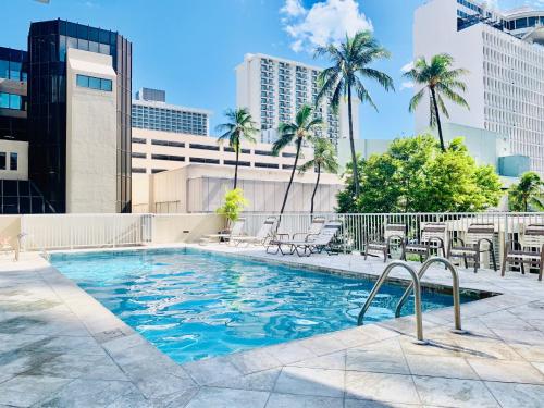 a pool with chairs and palm trees and buildings at Tropical Studios at Marine Surf Waikiki - FREE PARKING - BEST LOCATION - FULL KITCHEN - SWIMMING POOL in Honolulu